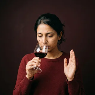 Priya Venkataraman smelling a glass of wine with one hand raised